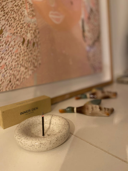 Incense burner with a single stick of incense on a surface, with a blurred background